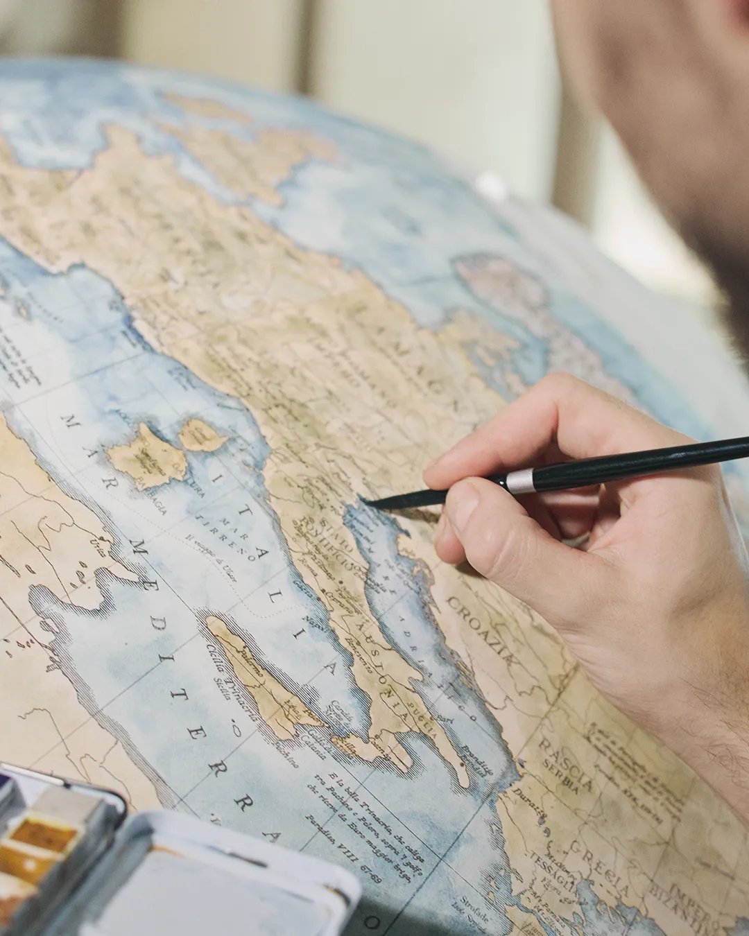 A brush laying watercolour along the Adriatic coast on a globe in progress