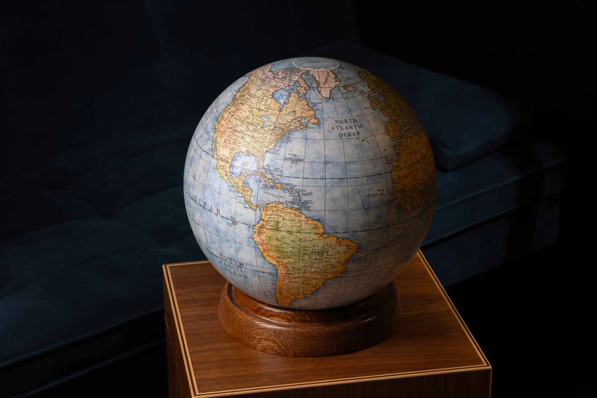 A terrestrial globe on its turned wooden base, on a walnut plinth in a darkened room