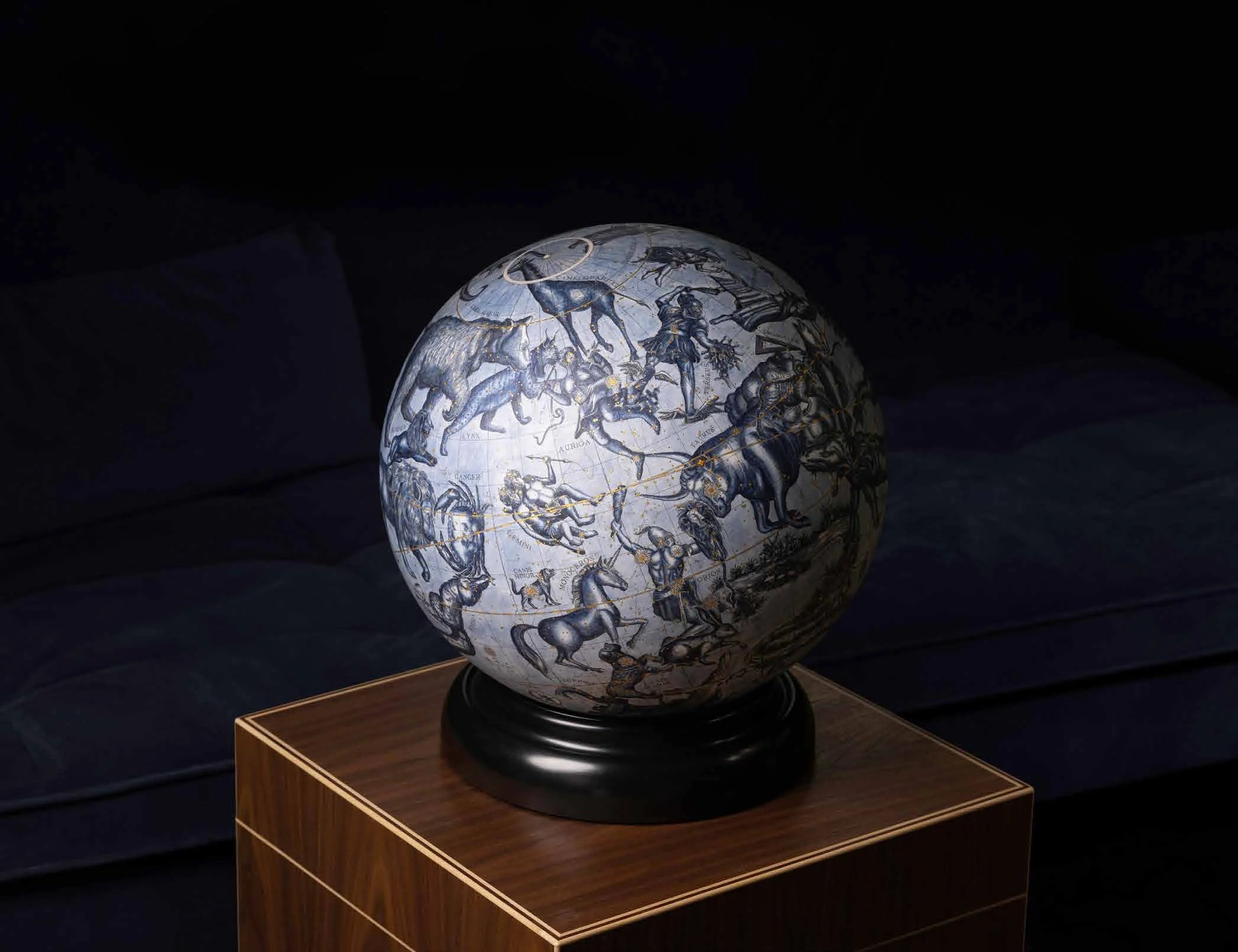 A celestial globe on its black base, on a walnut plinth in a darkened room